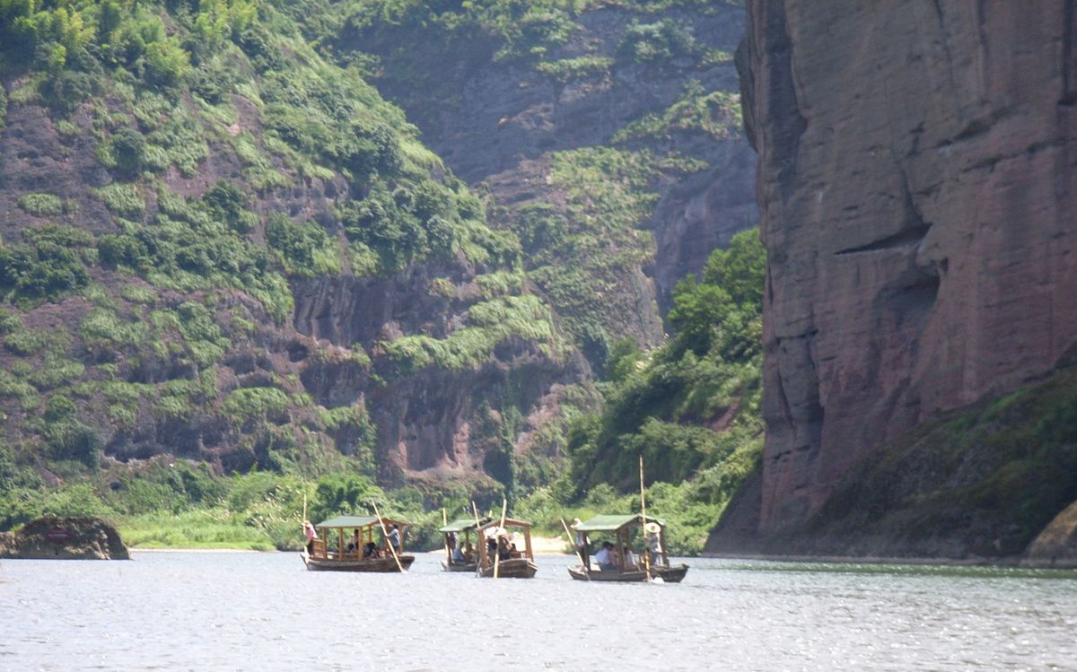A bamboo raft drifting down the Luxi River at Longhushan, past the red Danxia cliffs